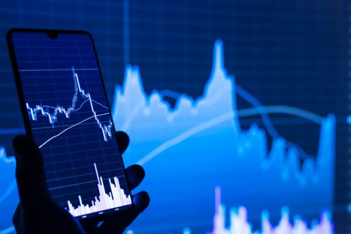 seseorang memegang ponsel di depan grafik saham
