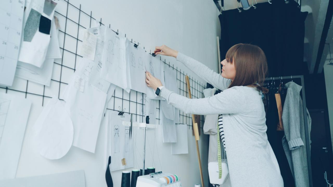 Seorang perancang busana sedang mengatur sketsa di dinding.